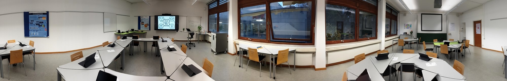 DigiLLab Raum mit Sitzplätzen und Tischen in verschiedenen Formationen mit iPads darauf und ein Bildschirm an der linken Wand